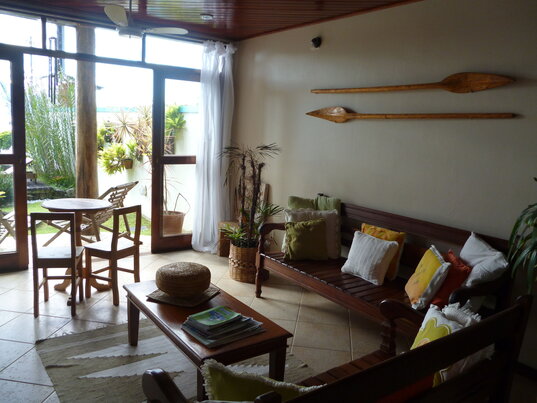 Gemütlicher Aufenthaltsbereich im Hotel Pousada Caiçara auf Ilha Grande, mit Holzmöbeln, farbenfrohen Kissen und dekorativen Paddeln an der Wand, der durch große Fenster viel Tageslicht erhält.