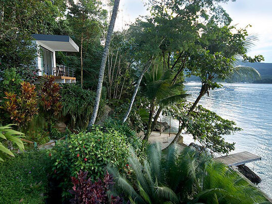 Tropische Umgebung des Hotel Asalem auf Ilha Grande, mit tropischer Vegetation, Palmen und einem Blick auf das ruhige Wasser, neben einem kleinen Steg und einer Terrasse.