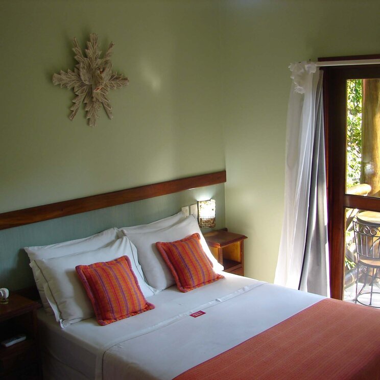 Zimmer in der Pousada Caiçara auf der Ilha Grande, Brasilien, mit gemütlichem Doppelbett und Zugang zu einem Balkon.