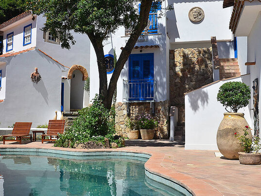 Pool im Innenhof des Hotels Vila da Santa mit weißen Gebäuden, blauen Fenstern und Bäumen in Búzios, Brasilien.