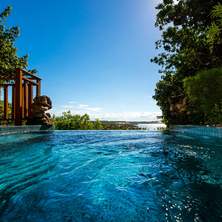 Infinity-Pool des Hotels Sombra e Água Fresca mit Steinstatuen und Meerblick in Pipa, Brasilien.