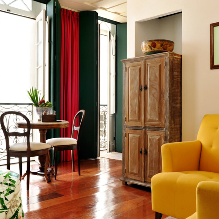 Suite mit gelben Sesseln, Holzschrank und hohen Fenstern mit roten Vorhängen im Hotel Villa Bahia.