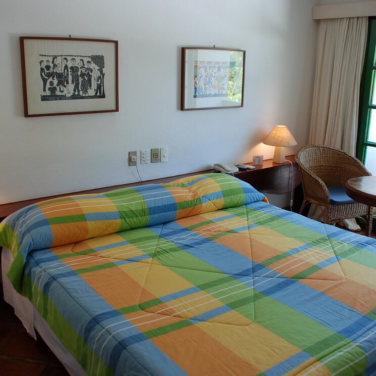 Ein modernes Zimmer im Hotel Sete Colinas in Recife, mit einem bequemen Bett, einem kleinen Tisch und Blick auf den Garten durch große Fenster.