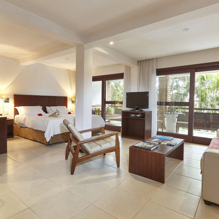 Master Suite im PortoBay Buzios mit Doppelbett, Sitzgruppe, TV und großem Balkonzugang mit Blick ins Grüne.