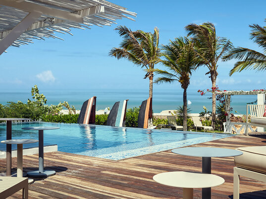 Poolbereich des Chili Beach Hotels auf einer Holzterrasse vor Palmen und Meerblick in Jericoacoara, Brasilien.