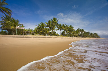 Breiter Sandstrand mit sanften Wellen und Palmenreihe vor der Pousada Encanto da Lua auf der Halbinsel Maraú, Brasilien.