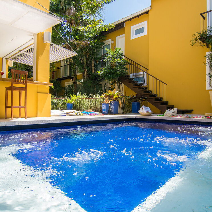 Poolbereich der Pousada La Chimére in Búzios, umgeben von bunten Pflanzen im gelben Innenhof.