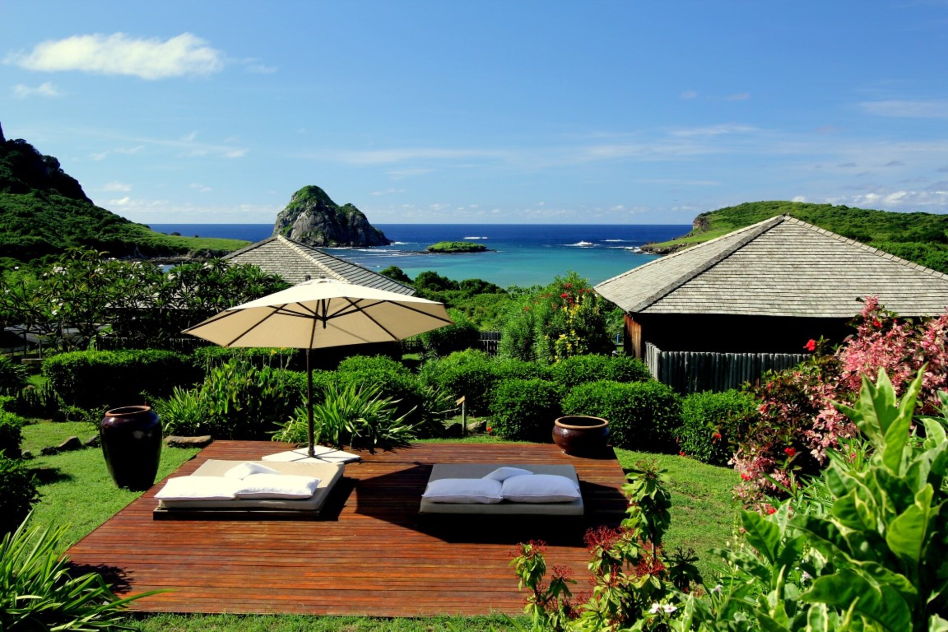 Entspannungsbereich im Garten der Pousada Maravilha in Fernando de Noronha, Brasilien, mit Liegen, Sonnenschirm und Blick auf das Meer.
