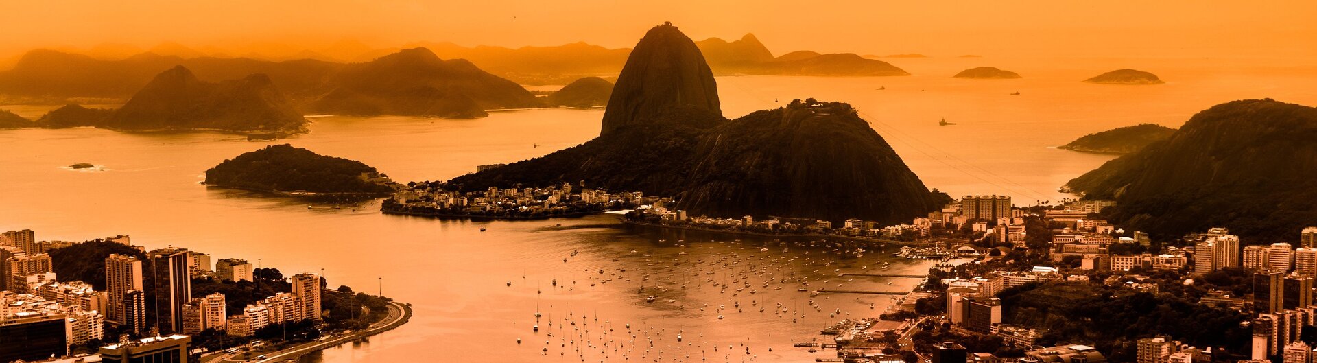 Der Zuckerhut in Rio de Janeiro leuchtet bei roter Abenddämmerung in warmen, goldenen Tönen.