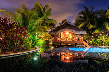 Beleuchteter Reetdach-Bungalow am Pool bei Nacht im Nannai Resort, Porto de Galinhas, Brasilien