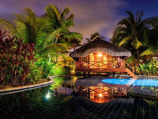 Beleuchteter Reetdach-Bungalow am Pool bei Nacht im Nannai Resort, Porto de Galinhas, Brasilien