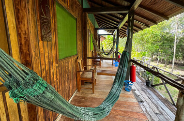 Lange Holzveranda mit mehreren grünen Hängematten vor den Zimmern im Amazon Village.