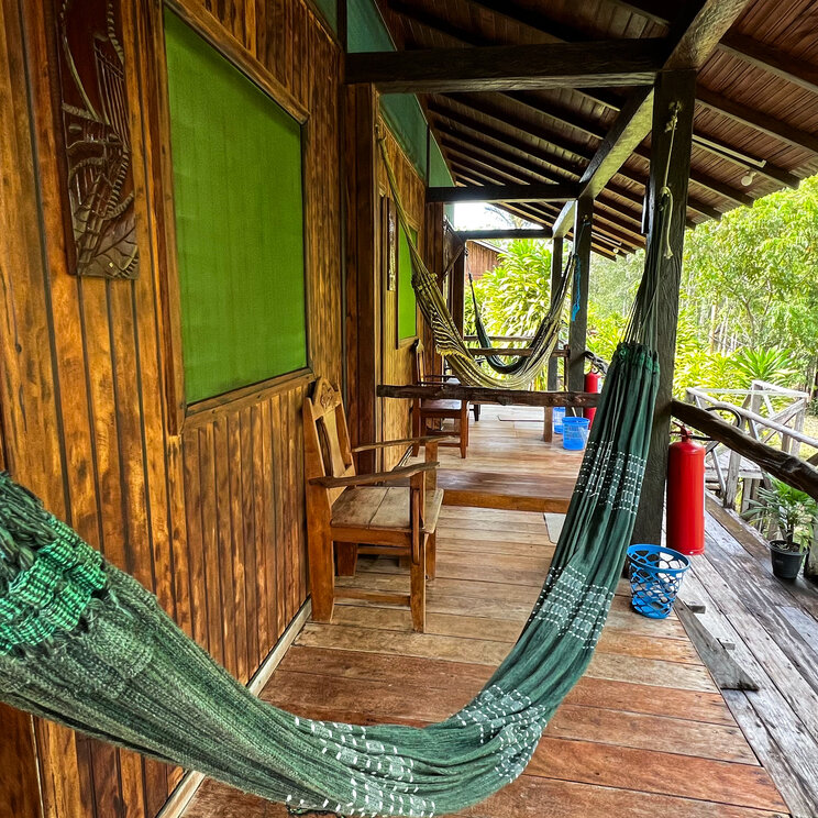 Lange Holzveranda mit mehreren grünen Hängematten vor den Zimmern im Amazon Village.
