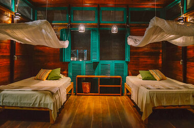 Beleuchtetes Twin-Zimmer mit Holzwaenden, gruenen Fensterlaeden und Moskitonetzen in der Uakari Lodge, Brasilien.