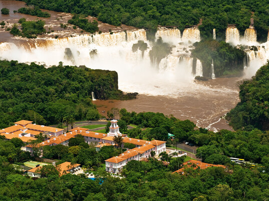 Luftaufnahme des Belmond Hotel das Cataratas, umgeben von Regenwald und mit Blick auf die beeindruckenden Iguaçu-Wasserfälle im Hintergrund.