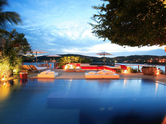 Der Pool im Hotel Insolito in Búzios bei Abenddämmerung, elegant und modern gestaltet, bietet einen herrlichen Blick auf die umliegende Landschaft und das Meer, umgeben von stilvollen Liegeflächen.