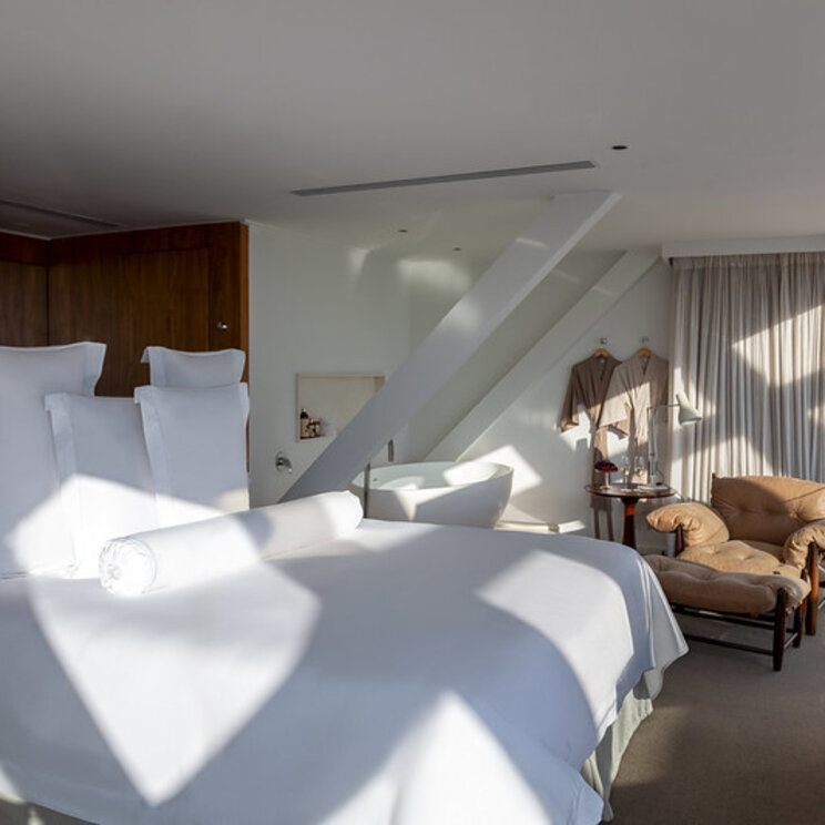 Modernes Hotelzimmer mit weissem Bett, Ledersessel und Blick auf die Stadt durch Lamellenfenster in Sao Paulo.