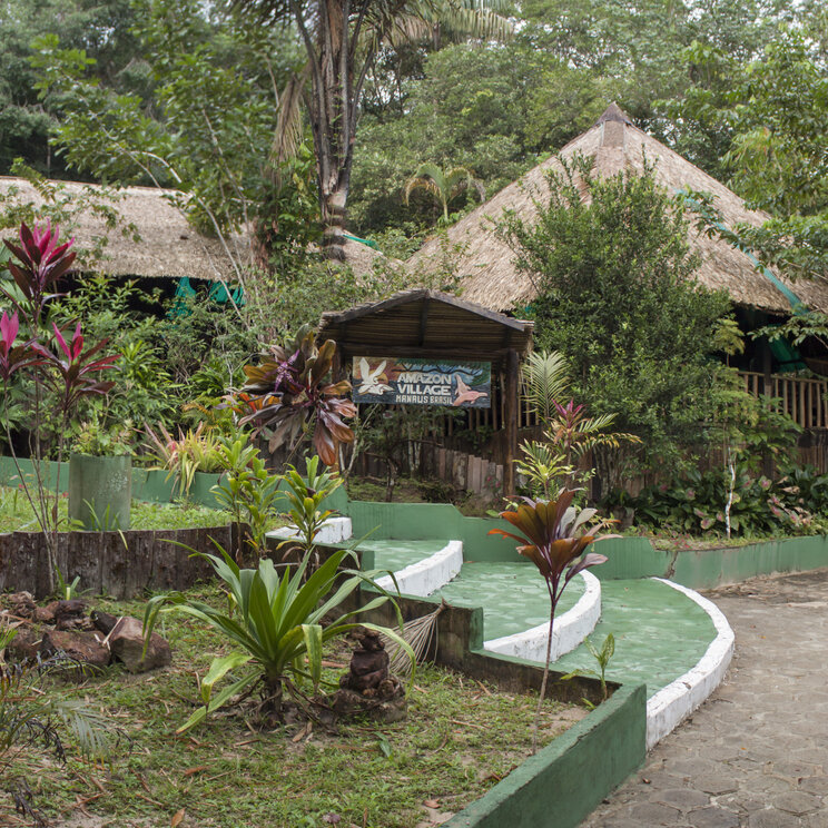 Tropischer Garten und Eingangsbereich mit Hinweisschild der Amazon Village Lodge in Brasilien.