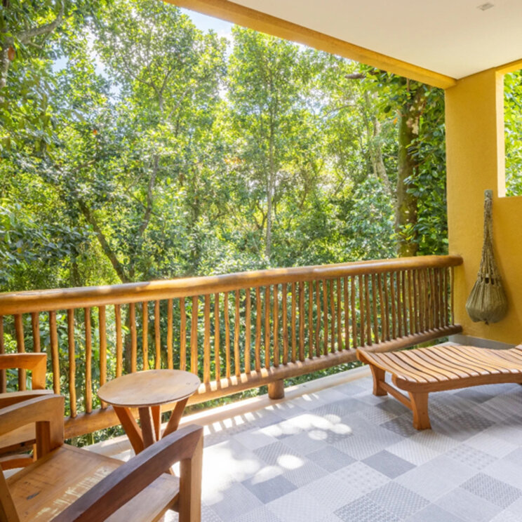 Balkon mit Holzliege und Stuhl vor dichten grünen Bäumen in der Pousada Naturalia, Ilha Grande, Brasilien.