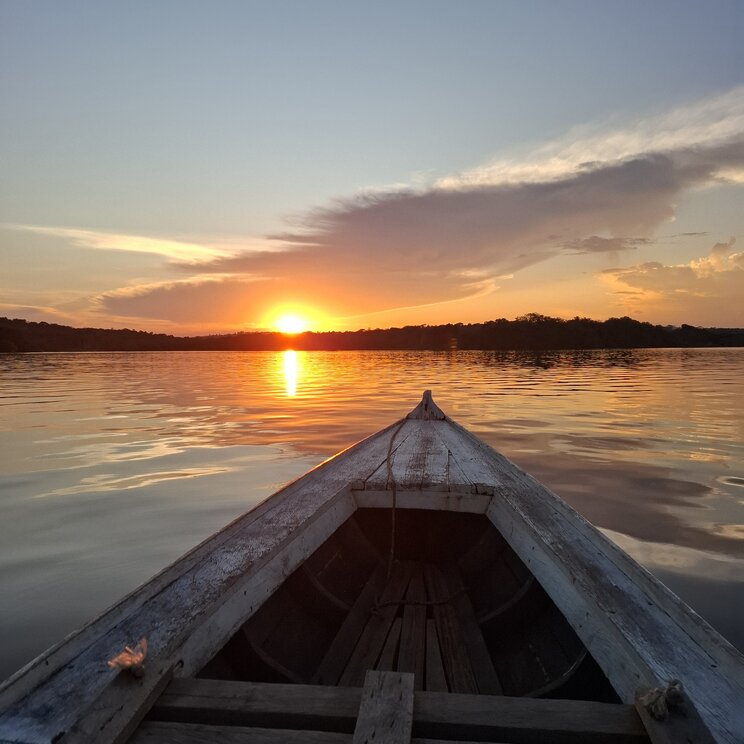 Blick vom Bug eines Holzbootes auf den Sonnenuntergang ueber dem Fluss nahe Amazon Village, Brasilien.