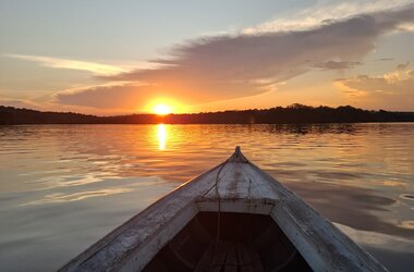 Blick vom Bug eines Holzbootes auf den Sonnenuntergang ueber dem Fluss nahe Amazon Village, Brasilien.