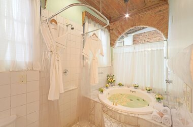 Helles Badezimmer mit Whirlpool unter einem gemauerten Rundbogen und weißen Bademänteln in Olinda.