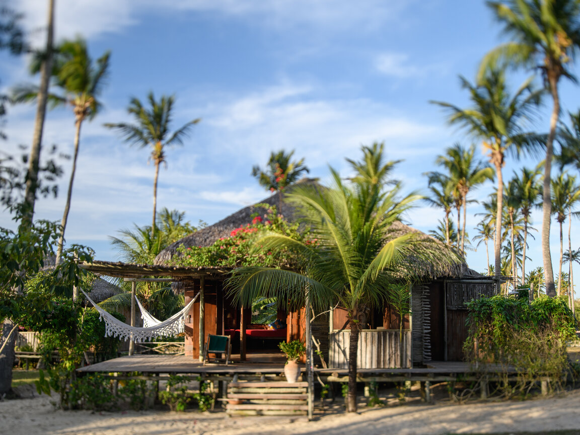 Holzbungalow mit Reetdach, Veranda und weiße Hängematte zwischen Palmen im Rancho do Peixe in Preá, Brasilien.