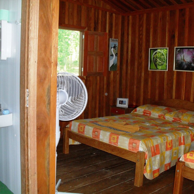 Die Unterkunft der Tariri Lodge im Amazonas, Brasilien, zeigt ein rustikales Zimmer mit Holzwänden, ausgestattet mit bunten Bettwäsche, einem Deckenventilator und einem Waschbecken im Raum.
