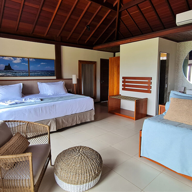 Helles Hotelzimmer mit Doppelbett, Holzdecke und großem runden Spiegel in einem Strand-Bungalow.