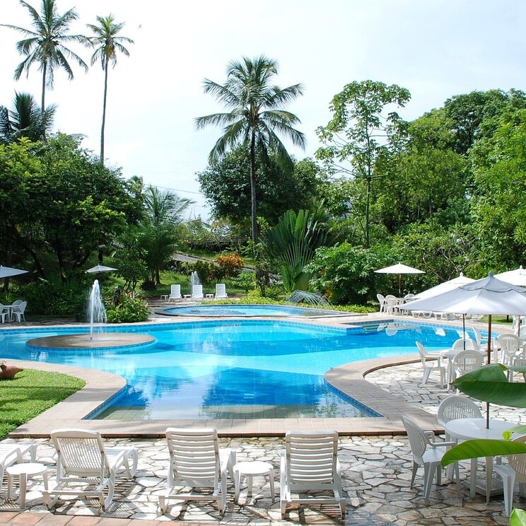 Ein einladender Poolbereich im Hotel Sete Colinas in Recife, umgeben von üppiger Vegetation, Liegen und Sonnenschirmen