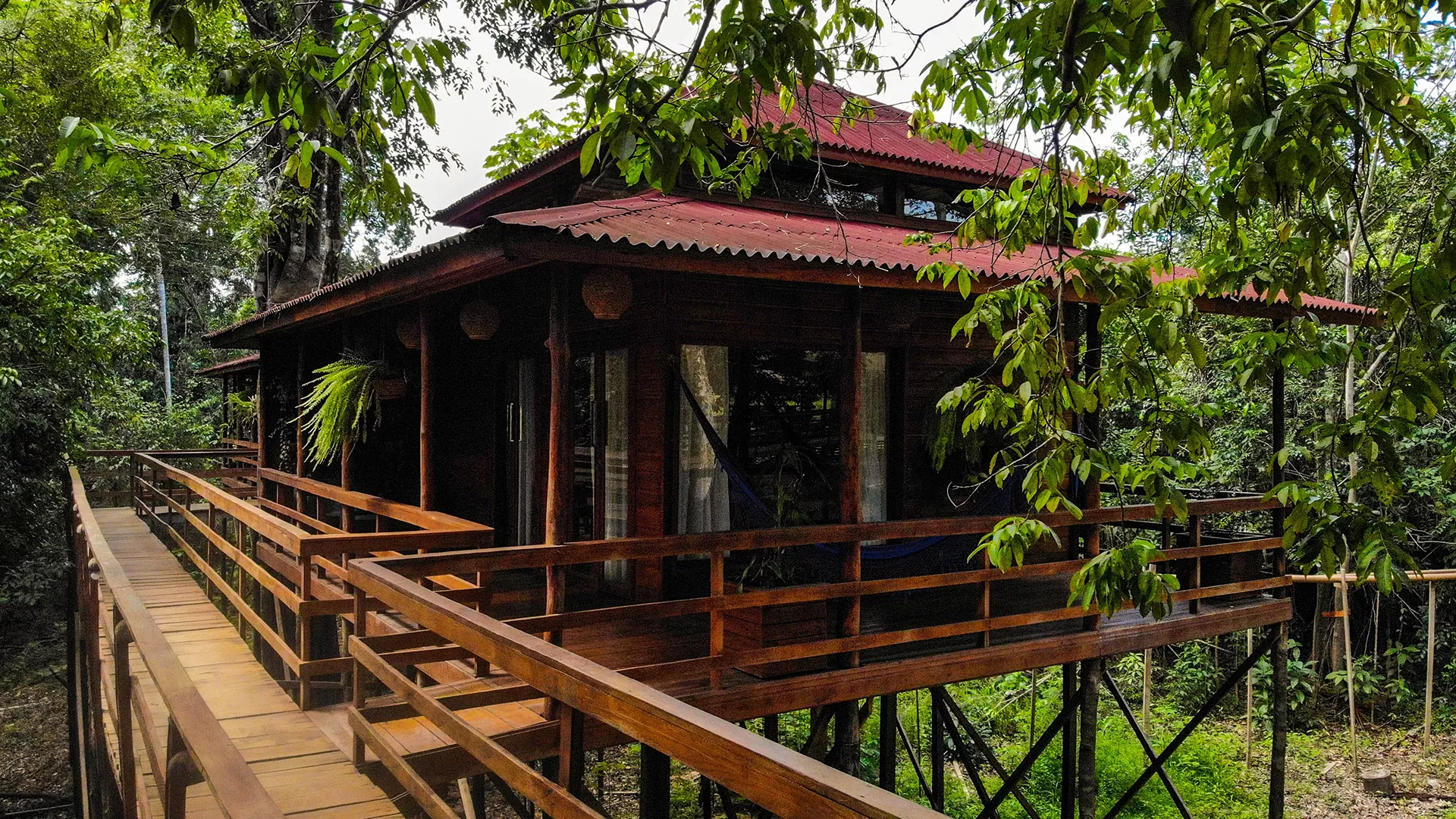 Holzhütte auf Stelzen in der Manati Lodge im Amazonas, Brasilien, umgeben von üppigem Grün und mit Verbindungswegen.